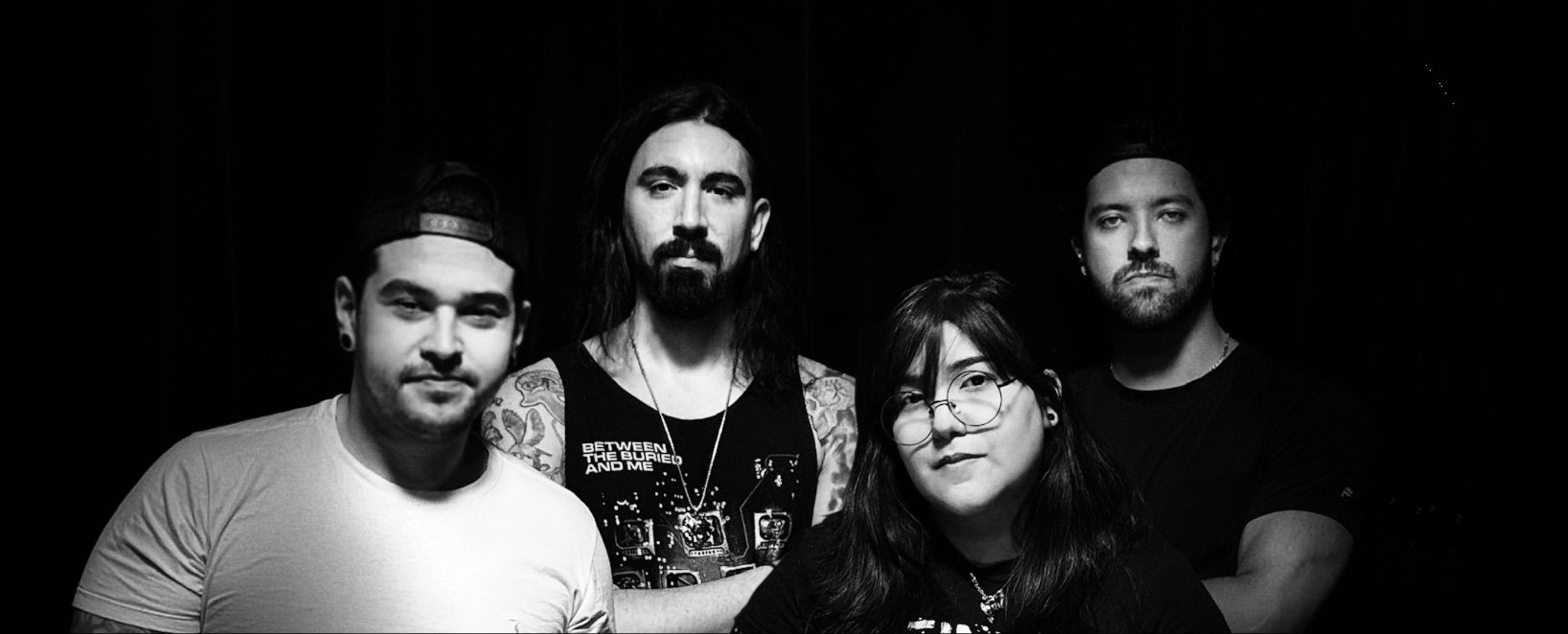 Black and white photo of four people posing together against a dark background